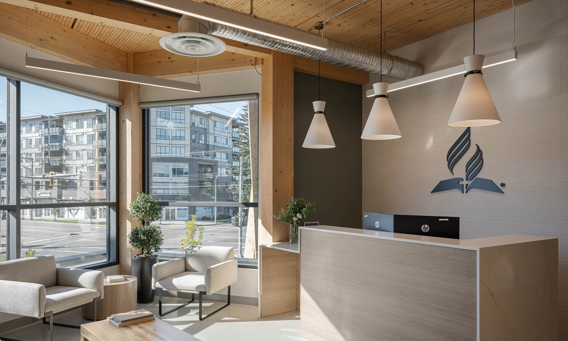 SDA reception with light wood tones, exposed timber ceiling, and Axis Lighting Sculpt grey suspended linear fixtures.