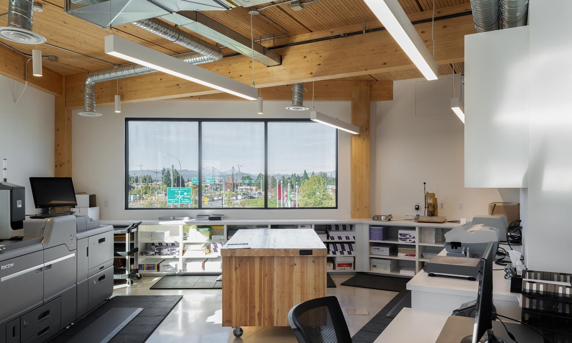 Open office interior with exposed mass timber ceiling and cable craft suspended lighting.
