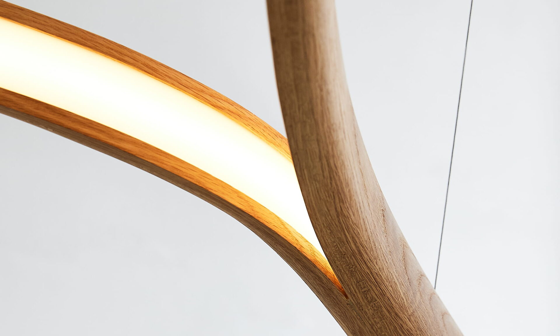 Close-up of the Poémia Pérola oak ceiling lamp, highlighting the curved, natural wood grain detail, and warm integrated LED glow.