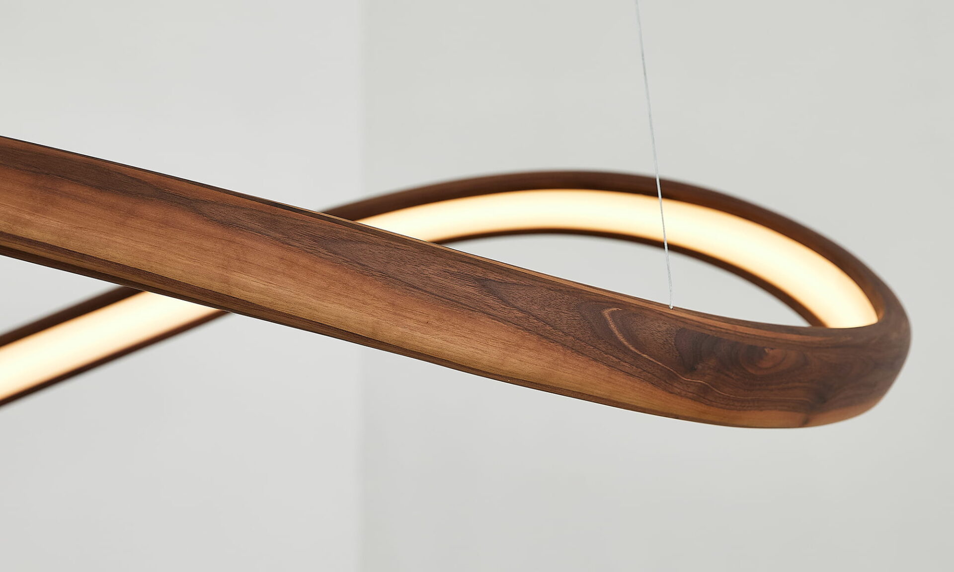 Close-up of the Poémia Horizonte walnut wood ceiling lamp, highlighting the layered, curved wood and warm integrated LED glow.