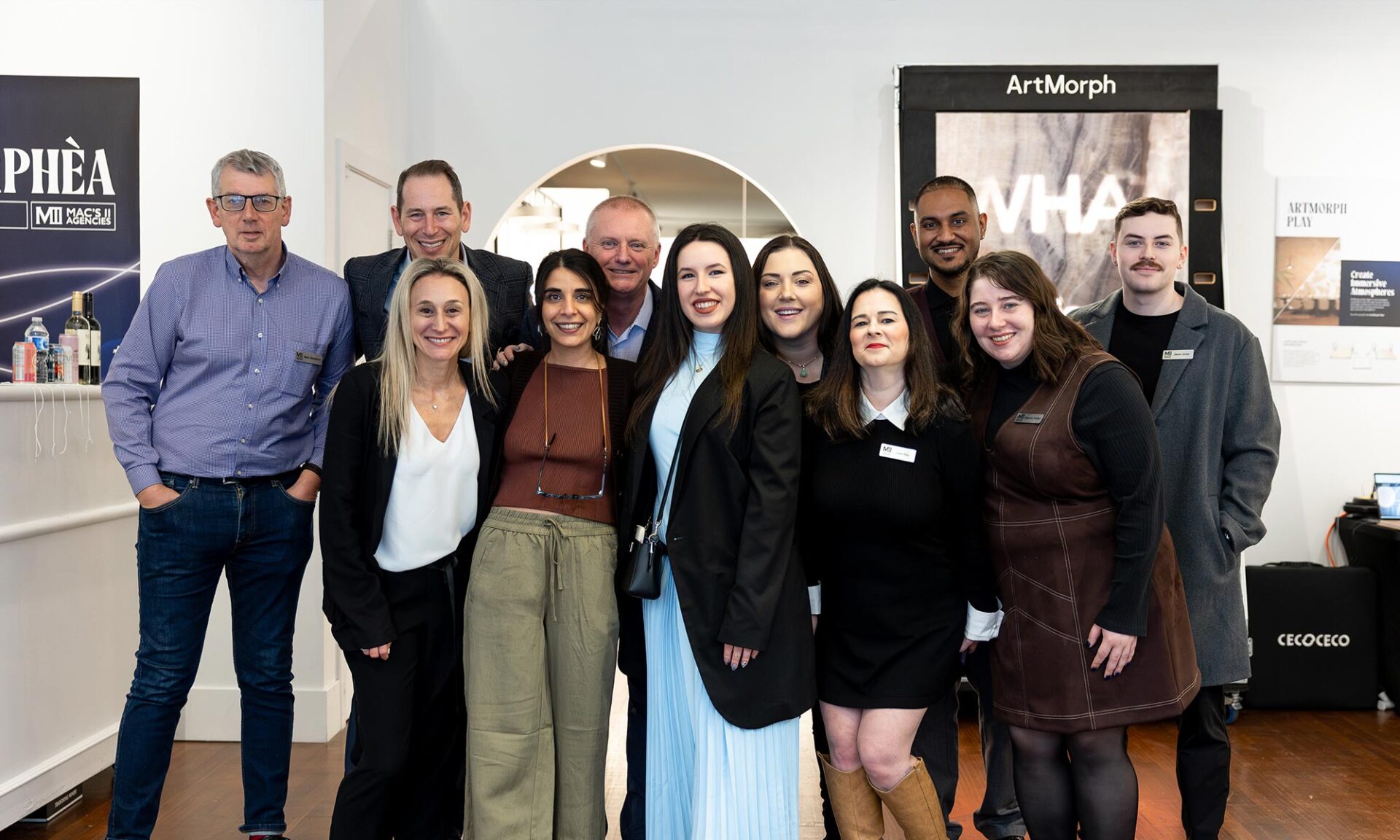 Group photo of the Mac’s II Agencies team at the Lumorphéa lighting exhibition inside The Gallery George in Vancouver, standing in front of the ArtMorph display and event signage.