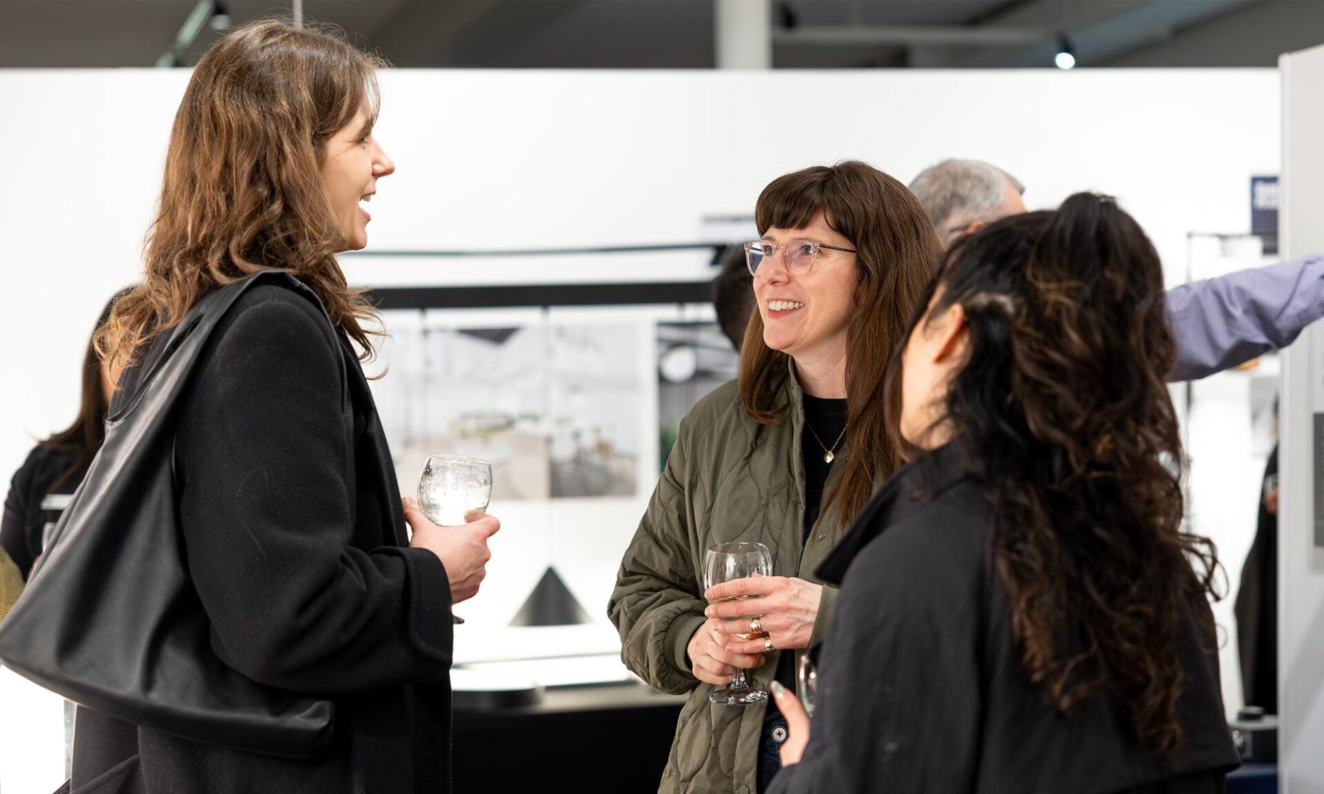 Three guests chatting at Lumorphéa inside The Gallery George in Vancouver, standing in front of the Axis Lighting display with illuminated fixtures behind them.