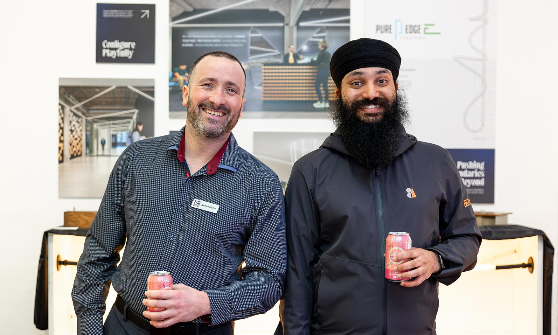 Two attendees pose in front of the PureEdge Lighting display at Lumorphéa in Vancouver, with PureEdge branding and exhibit photos on the gallery wall behind them.