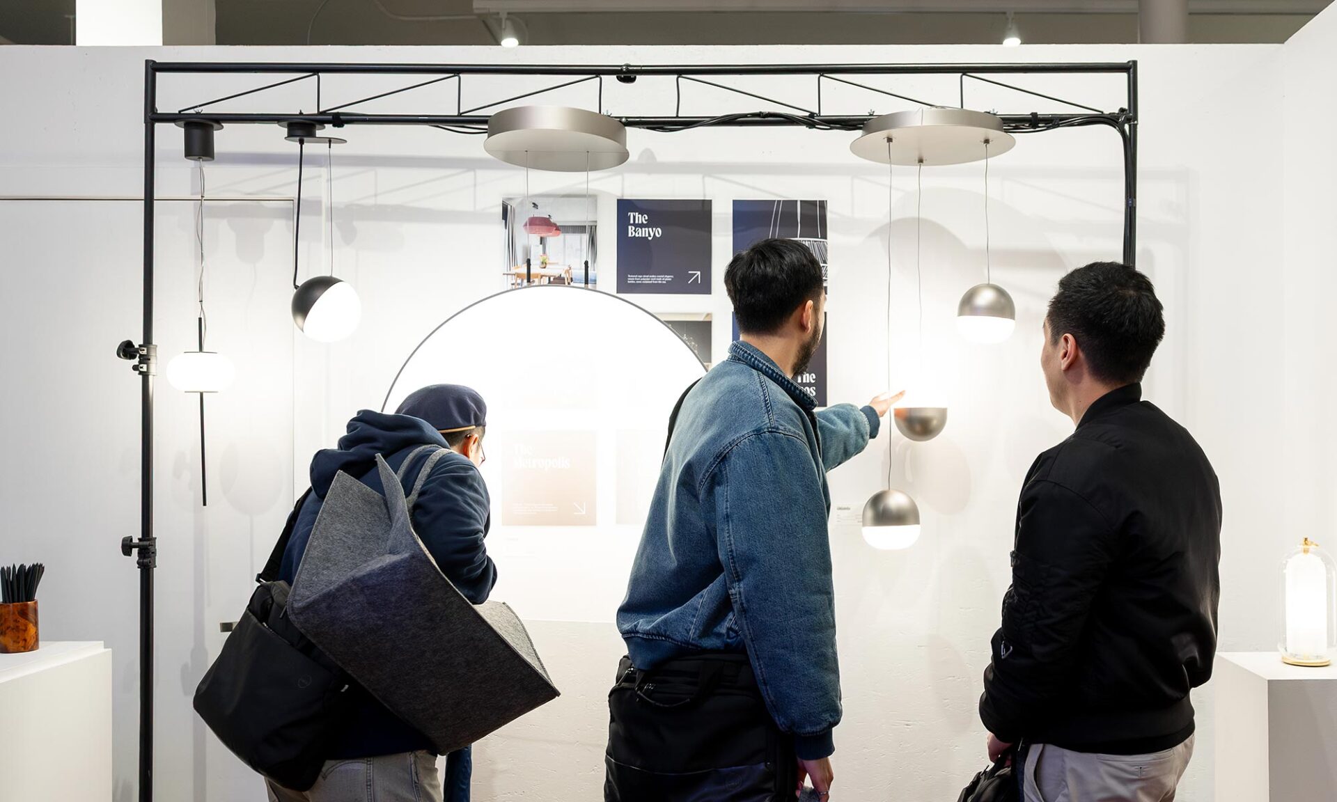 Guests viewing a Zaneen lighting display at Lumorphéa, with a black frame structure and multiple suspended pendants in front of a bright circular backlit panel inside The Gallery George in Vancouver.