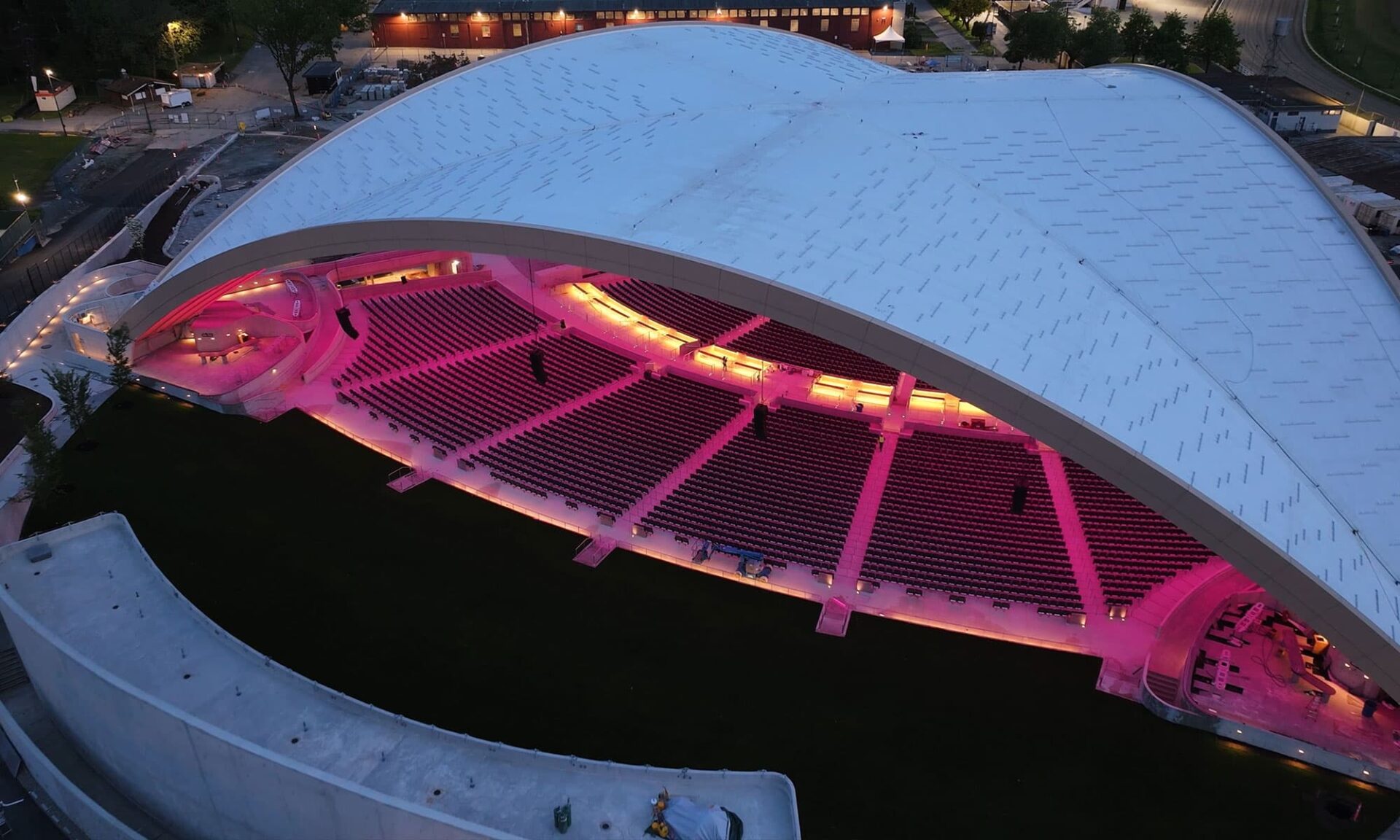 Downward exterior view looking into the PNE Amphitheatre Freedom Mobile Arch at night, showing the seating area with the interior illuminated in pink.