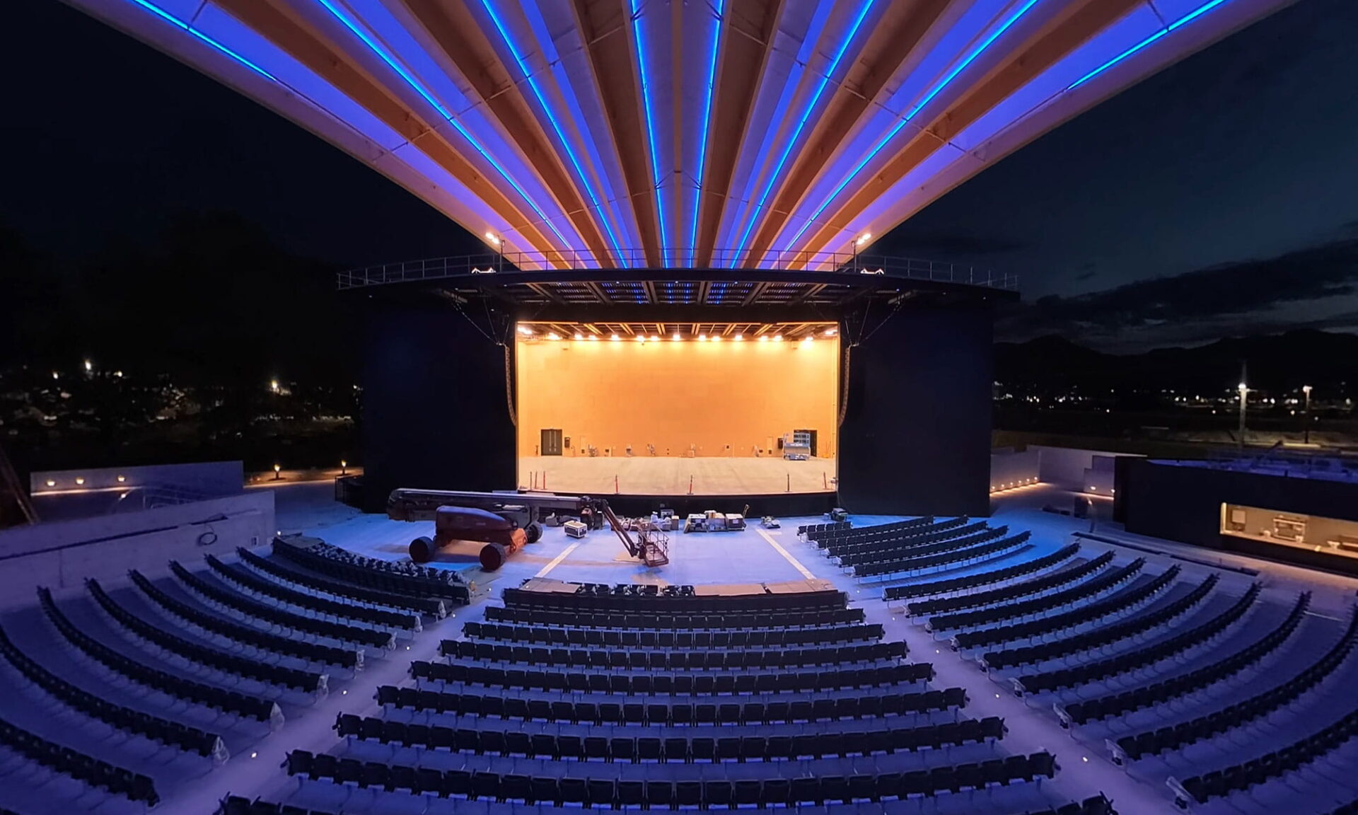 Nighttime interior view inside the PNE Amphitheatre Freedom Mobile Arch facing the stage, showing the mass timber roof illuminated in blue.