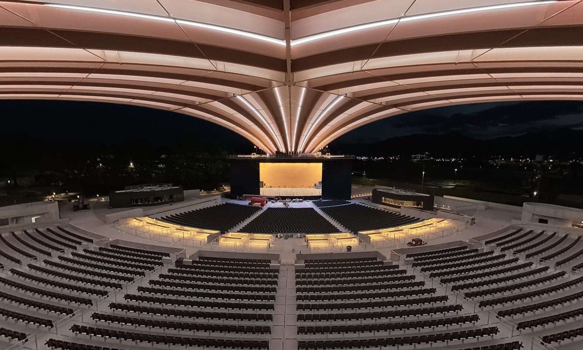Nighttime interior view from inside the PNE Amphitheatre Freedom Mobile Arch, facing the stage, with BL Lighting neonVIEW lighting illuminating the curved mass timber beams.