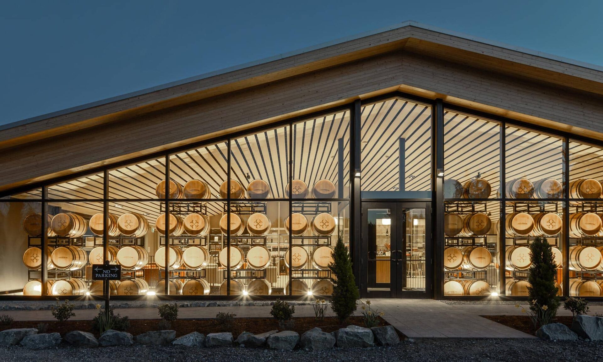Night exterior view of Unsworth Vineyards’ tasting room, with the illuminated barrel wall visible through the glazing.