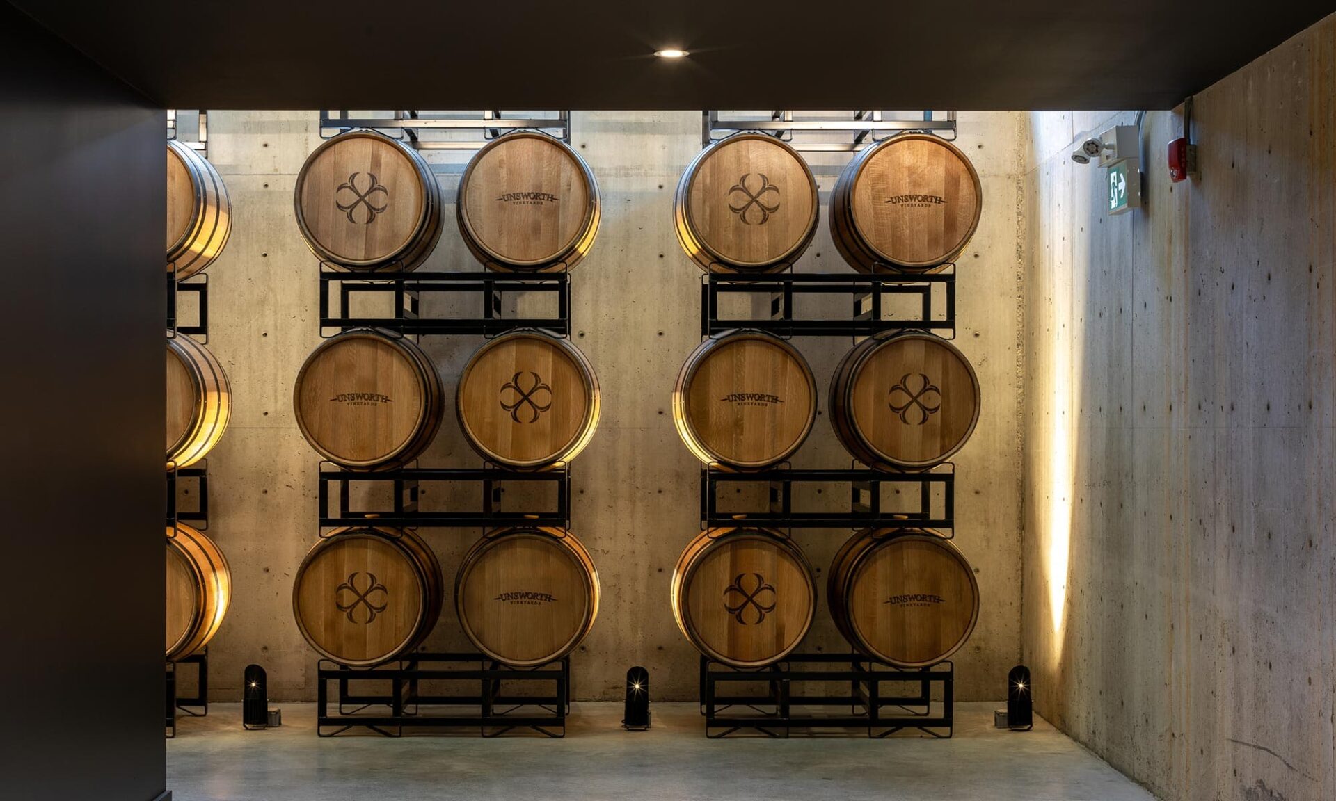 View from the lower floor entering the VIP barrel room at Unsworth Vineyards, showing a warm, softly illuminated glimpse of the barrel wall feature.